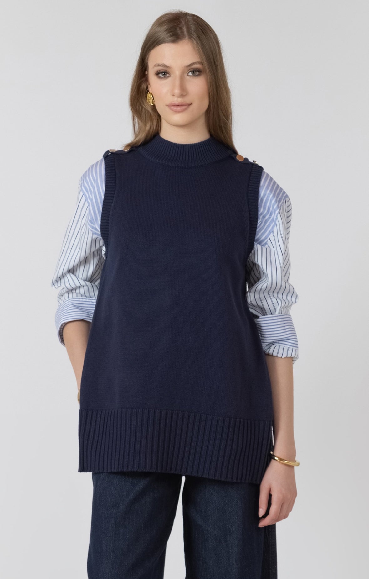 Woman wearing a navy sweater vest over a striped shirt on a white background