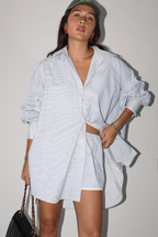 Woman wearing a white and blue striped shirt standing against a plain background.