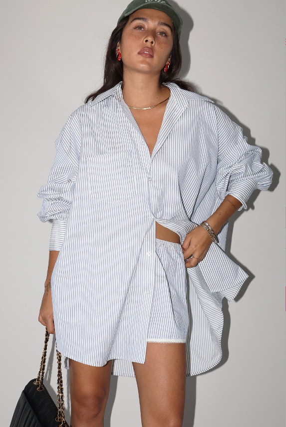 Woman wearing a white and blue striped shirt standing against a plain background.