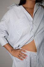 Person wearing a blue and white striped shirt with rolled-up sleeves on a plain background