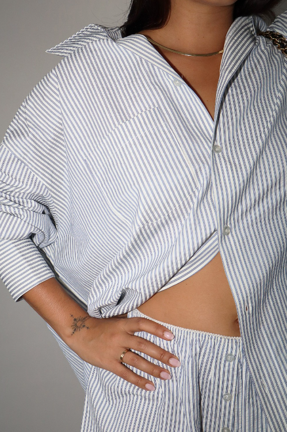 Person wearing a blue and white striped shirt with rolled-up sleeves on a plain background